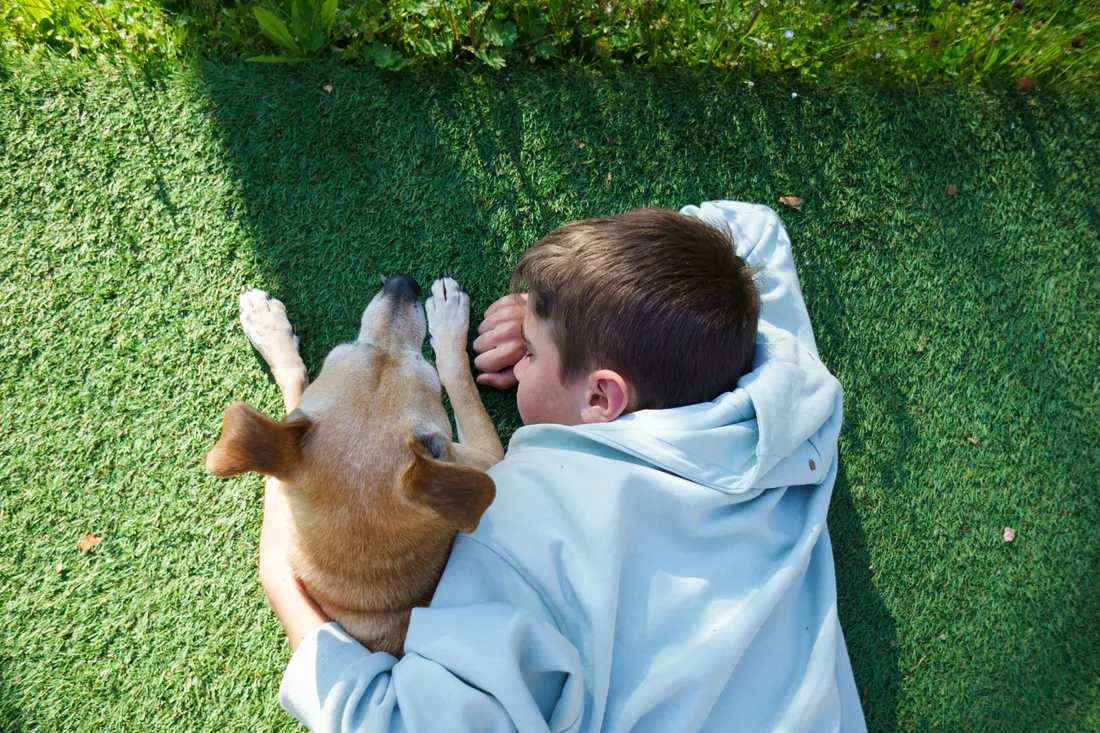 A boy and his dog relaxing together on backyard artificial turf